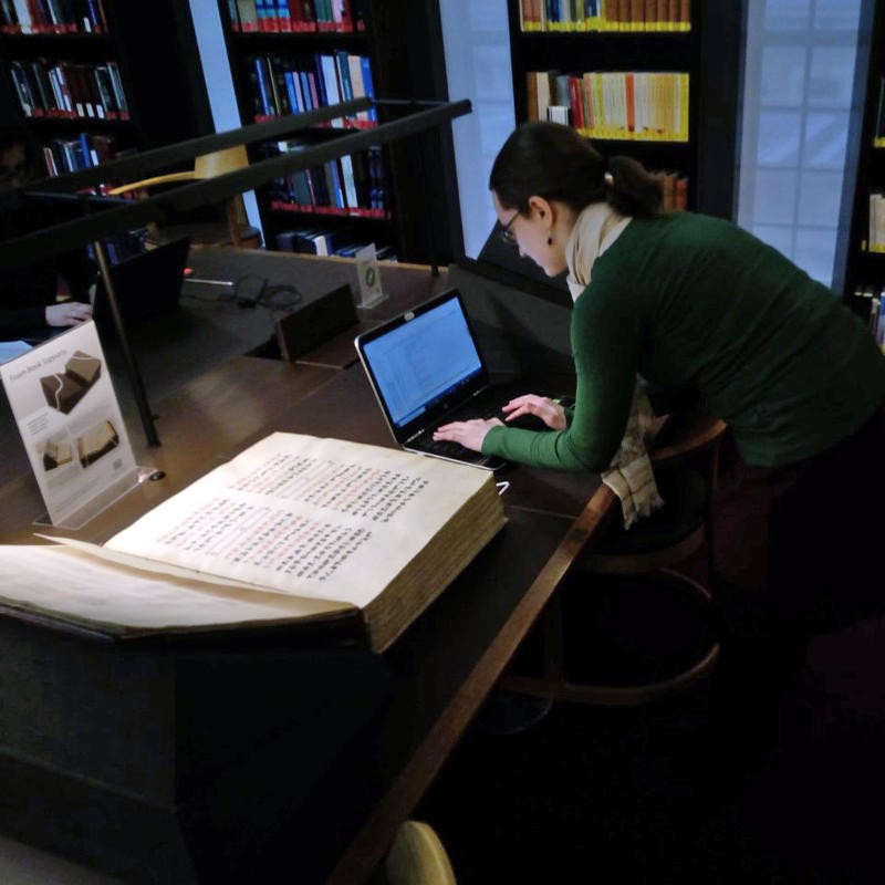 Fig 2 not a small book Figure 2. Member of the team studying a very large book. Each page is about 4 times the size of the team-member’s laptop, which is a small MacBook. The book seems more than 15 cm thick.