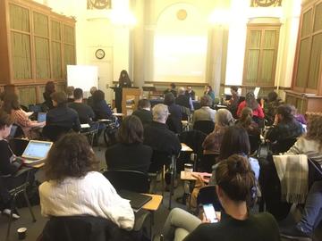 A conference room full of people sat down listening to a person give a talk